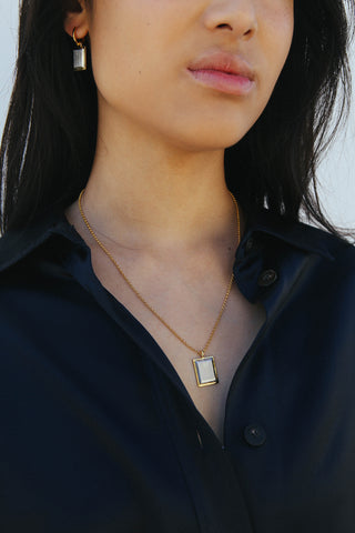 Model wears a navy blue shirt with earrings and a necklace featuring rectangular shape pendant, made from a two tone gold and silver finish.
