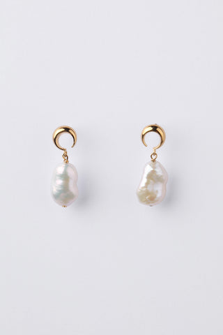 A pair of gold crescent moon shaped earrings, with a natural pearl hanging, on a light grey background.