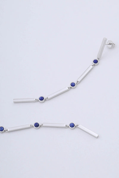Model wearing rhodium plated sterling silver long drop earrings by Miro Miro, featuring interlocking bars and natural lapis lazuli stones set in a bezel fitting.