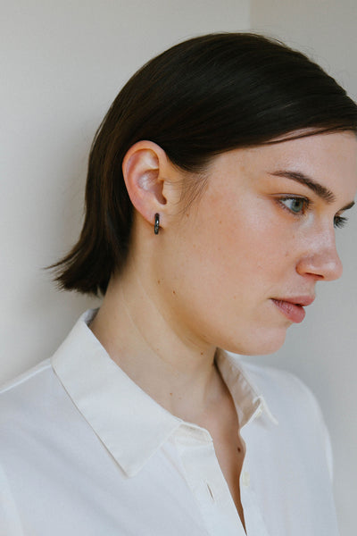 A woman in profile wearing a black hoop earring, shown from the chest up against a plain light background.