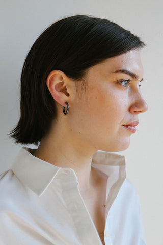 A woman in profile wearing a black hoop earring, shown from the chest up against a plain light background.