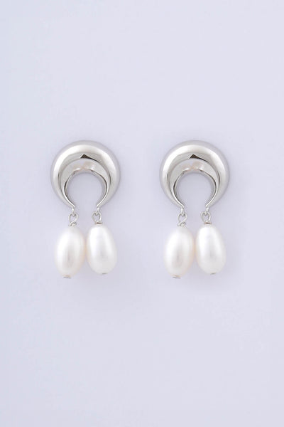 Model wears rhodium plated sterling silver plated earrings by Miro Miro, crafted in a crescent moon shape from which a pair of natural freshwater tear drop pearls hang.