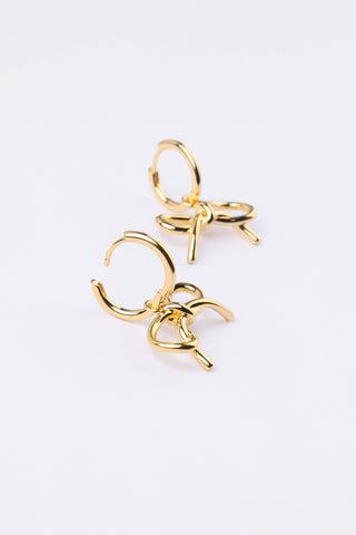 A pair of gold hoop earrings with a small bow-shaped charm attached, photographed on a clean white background.