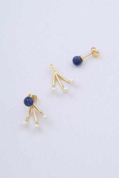 Model wears gold plated earrings by Miro Miro, featuring a spherical natural lapis lazuli stud, with a triple curved pronged backing from which hangs small freshwater pearls. Styled with a matching single lapis lazuli stud.