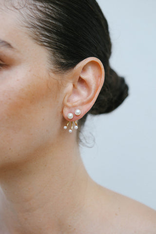 Model wears gold plated earrings by Miro Miro, featuring a natural freshwater pearl stud, with a triple curved pronged backing from which hangs small freshwater pearls. Styled with its matching single pearl stud.