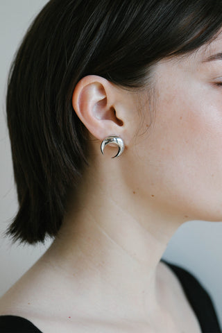 A close-up side profile of a person with short dark hair wearing a small silver crescent moon stud earring.