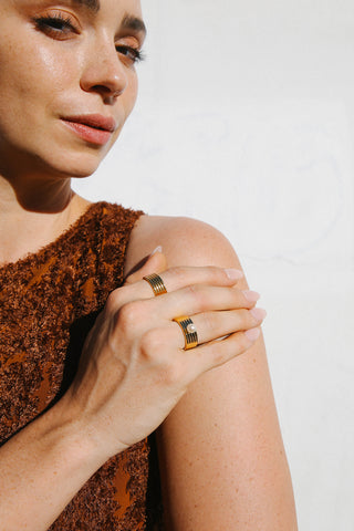 Model wears a brown textured dress and two gold plated rings by Miro Miro, one with a plain ribbed textural finish and the other with a singular pearl set on a thick band.
