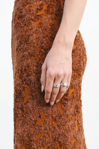 Model wears a brown textured dress and two rhodium plated sterling silver rings by Miro Miro, one with a plain ribbed textural finish and the other with a singular pearl set on a thick band.
