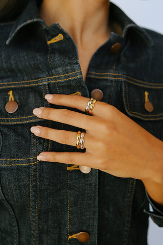 Model's hand wears four rings, two gold and two silver. Each ring is curved and bulbous.