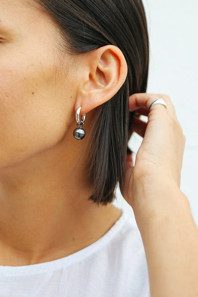 Close up of model wearing silver hoop earring with oxidised silver drop sphere.