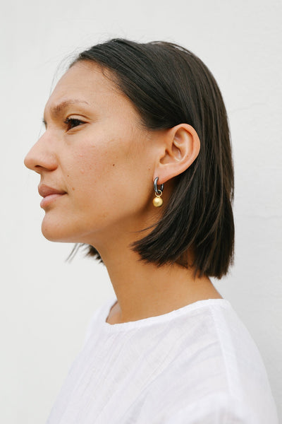 Model headshot wearing oxidised silver hoop earring with matte gold drop sphere