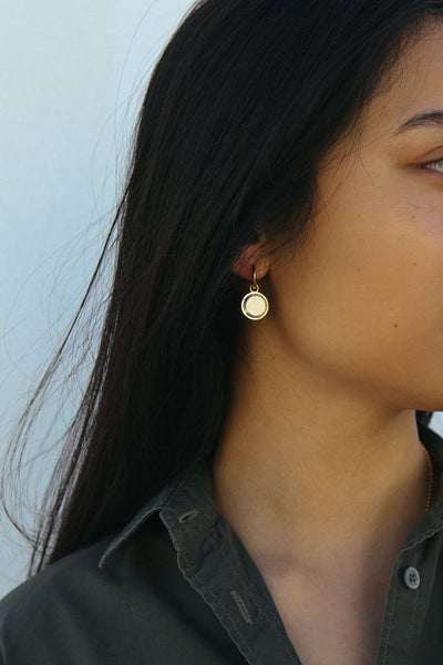 A detail image of an earring featuring a circular drop shape, made in a two tone silver and gold finish.