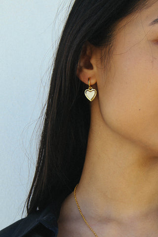 Detail shot of a heart shape drop earring, made in a two tone gold and silver finish.