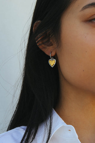 Detail shot of a heart shape drop earring, made in a two tone silver and gold finish.
