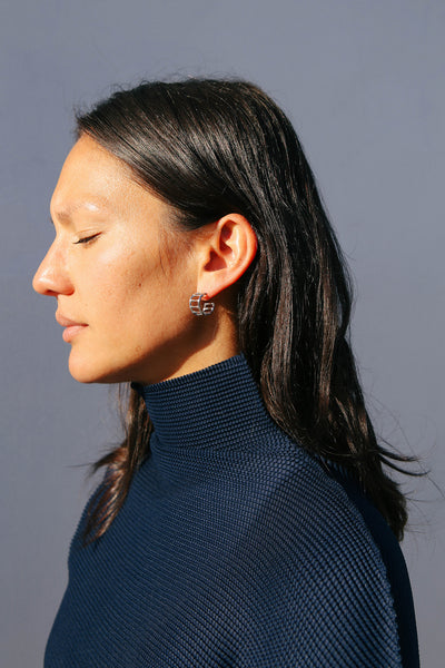 Close up of model wearing small silver hoops shaped like bamboo.