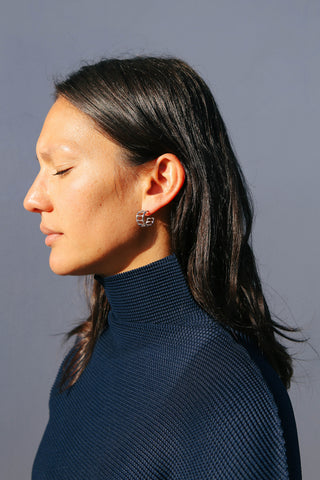 Model wears blue top and small silver hoop earrings shaped like bamboo.