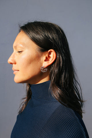 Model wears navy blue top and silver hoop earrings that resemble structural bamboo furniture.