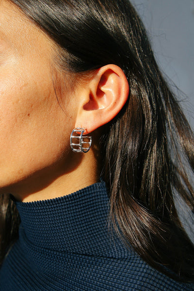 Model wears navy blue top and silver hoop earrings that resemble structural bamboo furniture.