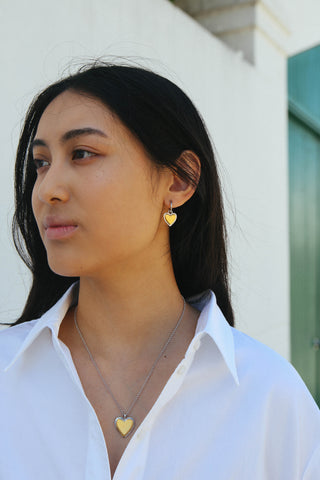 Model wears earrings and a necklace featuring heart shapes, made from a two tone silver and gold finish.