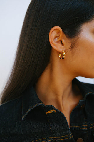 Model wears denim jacket and chunky, bulbous gold hoop earrings.