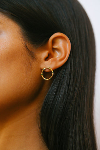 Detail shot of ear with front facing circular gold earrings, made up of bamboo segments, with green crystals in between them.