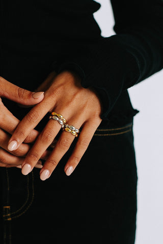 Close up of model's hand wearing four rings, two silver and two gold, each chunky and bulbous in shape.