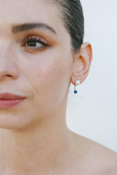 Pair of rhodium plated sterling silver earrings by Miro Miro, showing a freshwater pearl stud and a removable ear jacket from which hangs a natural lapis lazuli stone.