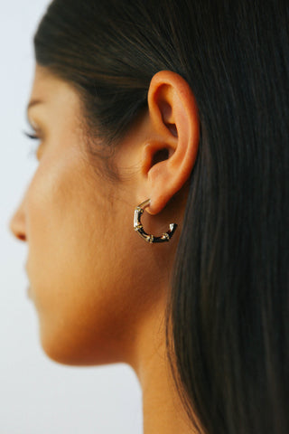 Detail shot of ear wearing bamboo shaped silver hoop earrings with small yellow crystals between each node.