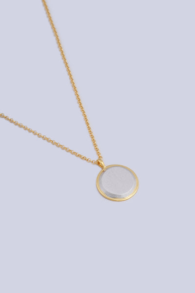 A necklace featuring a circular shape pendant, made from a two tone gold and silver finish.