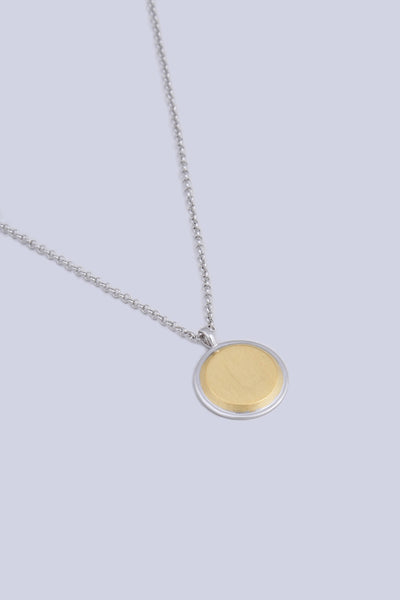 A necklace featuring a circular shape pendant, made from a two tone silver and gold finish.