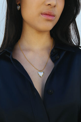 Model wears a blue shirt and a necklace featuring a heart shape pendant made from a two tone gold and silver finish.