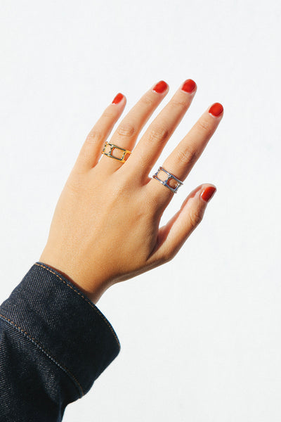 Hand with red nail polish wearing two rings, one gold and one silver.